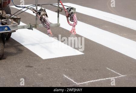 Stadtarbeiter malen Straßenübergangsspuren. Lackiermaschine lackiert Streifen auf Asphalt für Fußgänger. Stockfoto