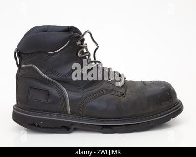 Ein alter, abgetragener, schwarzer Arbeitsstiefel aus Leder mit einer gerissenen Gummisohle wird von der Seite isoliert gegen weiß dargestellt. Stockfoto