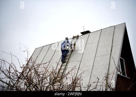Der Dachdecker klettert die Leiter hinauf zum Dach Des Hauses, um Blechdach zu befestigen Stockfoto