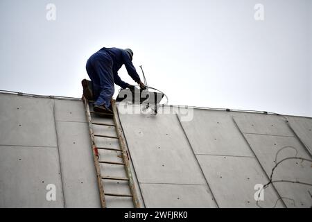 Ein Schornstein klettert auf eine Leiter zum Dach, um einen Schornstein zu reparieren Stockfoto