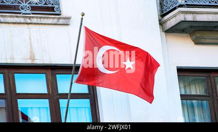 Türkische Flagge winkt im Wind an einem traditionellen Haus mit Fenstern. Nahaufnahme des Putenbanner, das weht, weiche und glatte Seide. Stoffstruktur ensig Stockfoto