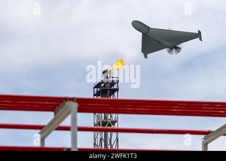 Eine Militärdrohne fliegt über eine Ölraffinerie und brennt Feuer. Stockfoto