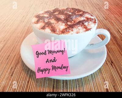 Guten Morgen und Happy monday Text geschrieben auf einem Haftnotiz mit heißer Schokolade auf einem Holztisch. Stockfoto