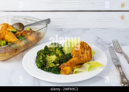 Abendessen. Nahaufnahme eines Tellers mit einem im Ofen gebackenen Hähnchenkegel und Brokkoli, serviert mit frischem Salat auf hellem Marmorhintergrund Stockfoto