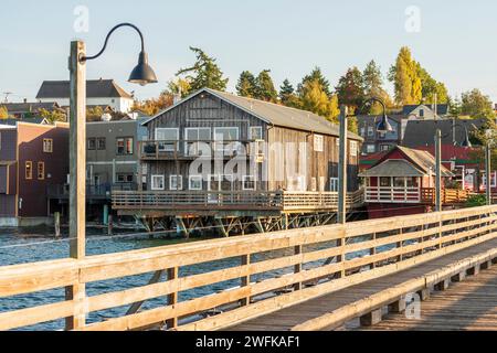 Historische Holzgebäude auf Pfählen, umgeben von bunten Bäumen des Herbstes, ragen in der Penn Cove in Coupeville, Whidbey Island, ins Wasser. Stockfoto