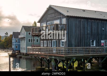 Horizontales Foto von historischen Holzgebäuden, die auf Pfählen gebaut wurden und in der Penn Cove in Coupeville, Whidbey Island, Washington, ins Wasser ragen. Stockfoto