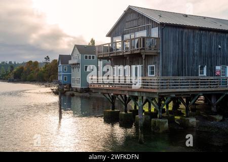 Horizontales Foto von historischen Holzgebäuden, die auf Pfählen gebaut wurden und in der Penn Cove in Coupeville, Whidbey Island, Washington, ins Wasser ragen. Stockfoto