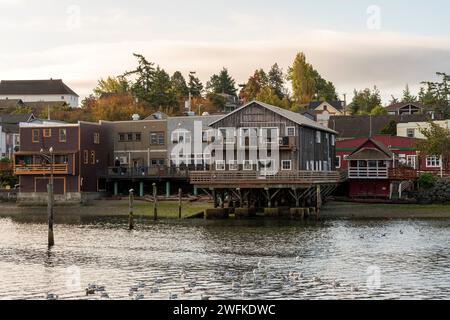 Horizontales Foto von historischen Holzgebäuden, die auf Pfählen gebaut wurden und in der Penn Cove in Coupeville, Whidbey Island, Washington, ins Wasser ragen. Stockfoto