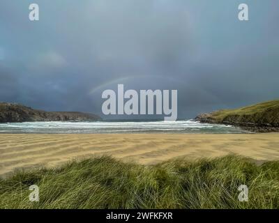 Ein Regenbogen über dem wunderschönen und abgeschiedenen Cliff Beach in der Nähe des Dorfes Bhaltos auf der Isle of Lewis in den Äußeren Hebriden an einem stürmischen Tag Stockfoto