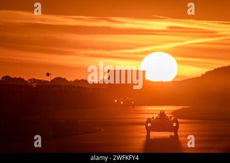 Die untergehende Sonne auf dem Goodwood Motor Circuit zeigt einen Teilnehmer am Freddie March Memorial Trophy Abendrennen Stockfoto