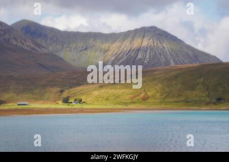 Blick über Loch Ainort auf die Berge dahinter und ein einzelnes Farmhaus und Schuppen an der Seite des Loch auf der Isle of Skye in Schottland. Stockfoto