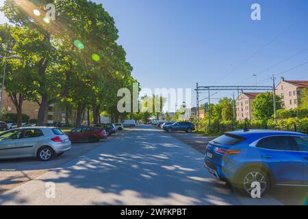 Ein malerischer Blick auf eine Straße mit Parkplatz auf beiden Seiten, Grün, das die Bahngleise trennt, und Wohnhäuser. Uppsala. Schweden. Stockfoto