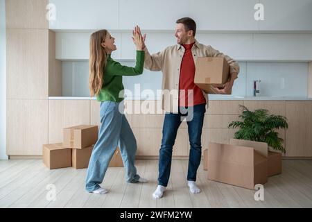 Ein Mann gibt fünf an eine lächelnde Frau, die einen Karton trägt, der in eine neue Wohnung zieht. Umzug. Stockfoto
