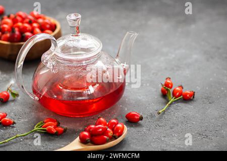 Hagebuttentee in einer Teekanne, Kräutertee Heilpflanzen mit Hagebuttenfrüchten auf rustikalem Tisch. Dogrose Winter Tee Hintergrund Stockfoto