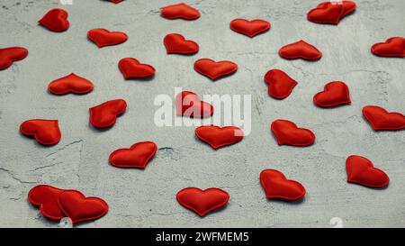 Viele rote Seidenherzen auf strukturierter grauer Oberfläche, selektiver Fokus. Konzept von Liebe, Romantik, Valentinstag Stockfoto