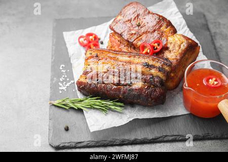 Gebackene Schweinebauchstücke, serviert mit Sauce, Rosmarin und Chili auf grauem Tisch Stockfoto