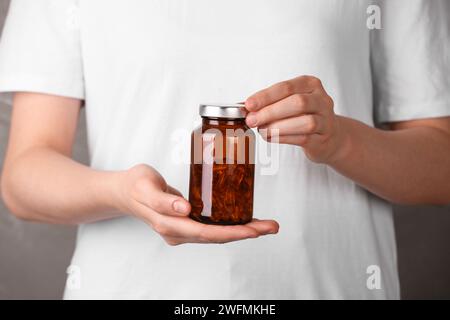 Frau, die Flasche mit Vitaminkapseln vor hellbraunem Hintergrund hält, Nahaufnahme Stockfoto