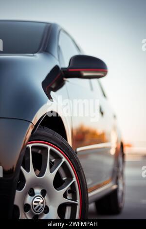 Black Golf GTi parkte auf einem großen, leeren Asphaltparkplatz mit den Rädern nach rechts. Vorderradansicht links der kompakten sportlichen Volkswagen Heckklappe Stockfoto
