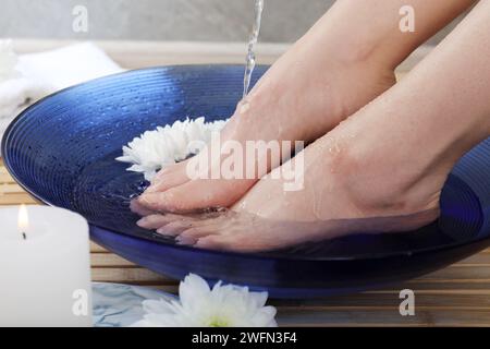 Frau, die Wasser auf ihre Füße gießt, in einer Schüssel auf dem Boden, Nahaufnahme. Spa-Behandlung Stockfoto