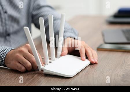 Mann, der Kabel in den WLAN-Router an einem Holztisch drinnen steckt, Nahaufnahme Stockfoto