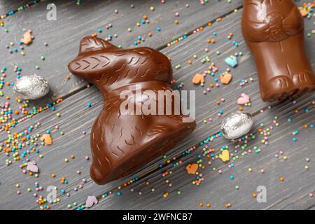 Schokoladenhasen, Ostereier in Folie und Streusel auf grauem Holzhintergrund Stockfoto