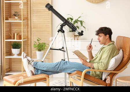 Junger Mann mit Teleskop und Notizbuch, der im Sessel sitzt Stockfoto