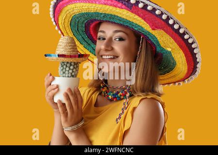 Hübsche junge Frau in Sombrero mit Kakteen auf gelbem Hintergrund Stockfoto