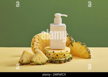 Leere Etikettenflasche in weißer Farbe, dekoriert mit Ananasscheiben (Ananas comosus) auf hellem Hintergrund. Ananas hat viele Vorteile für Haut und Haar Stockfoto