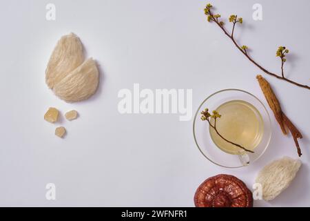 Essbares Vogelnest, Steinzucker, Lingzhi-Pilz, Ginseng und transparenter Becher mit Vogelnestsuppe auf weißem Hintergrund. Leerstelle für Produkt-Prese Stockfoto