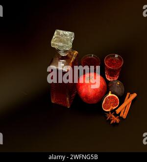 Feigen-Granatapfellikör mit Zimt und Anis auf schwarzem Hintergrund, hausgemachter Alkohol in Kristallgläsern und Gewürzen. Draufsicht, flach. Stockfoto