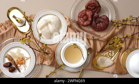 Viele Arten von Kräutern, Lingzhi-Pilzen, Jujube, Cordyceps und Ginseng, die auf einer goldenen Tischdecke mit Speisevogelnest und Vogelnestsuppe präsentiert werden. Kom Stockfoto