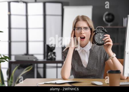 Schockierte junge Geschäftsfrau mit Wecker am Tisch im Büro. Zeitmanagement-Konzept Stockfoto