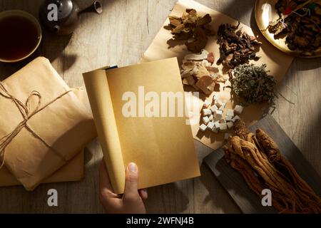 Ein Handmodell mit alten chinesischen Medizinbüchern mit vielen Kräutern, Medizinpackungen, einer Schüssel Medizin und einem irdenen Topf dahinter. Kraut Stockfoto