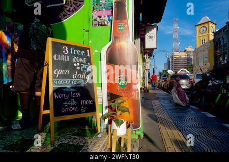 Vor einem der zahlreichen Ganja (Weed, Marihuana) Cafés in der Altstadt von Phuket Town, Thailand, das Wahrzeichen Phromthep Clocktower im b/g Stockfoto