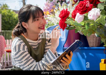 Eine charmante junge asiatische Mitarbeiterin im Blumengeschäft überprüft in ihrem Laden den Bestand an frischen Blumen. Konzept für kleine Unternehmen Stockfoto