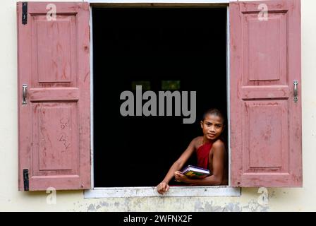 Junge buddhistische Mönche schauen aus dem Klosterfenster in Mrauk-U, Myanmar. Stockfoto