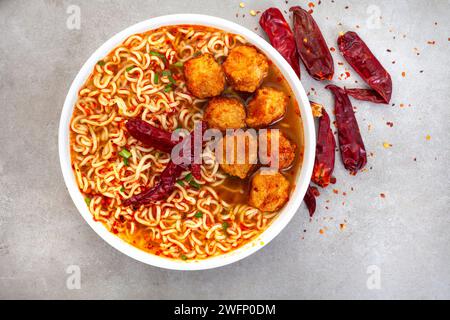 Scharfe Instant-Nudeln oder Ramen mit Fischbällchen und getrocknetem Chili auf meliertem grauen Hintergrund mit Kopierraum. Flache Lage, Draufsicht. Stockfoto