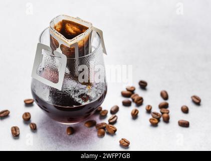 Ein Glas frisch gebrühten Tropfkaffee. Tropfkaffee-Beutel mit gemahlenem Kaffee zum Brühen in einem Glas Stockfoto