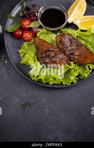 Stücke von gegrilltem Bio-Thunfisch auf schwarzem Keramikgericht mit Salat auf einem Tisch Stockfoto