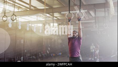 Bild der Datenverarbeitung auf der Schnittstelle über das Cross-Training von birassischen Männern mit Turnringen im Fitnessstudio Stockfoto