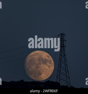 Vollmond, der zur blauen Stunde hinter dem Hügel aufsteigt und die Silhouette der Laternenpfahl bildet Stockfoto