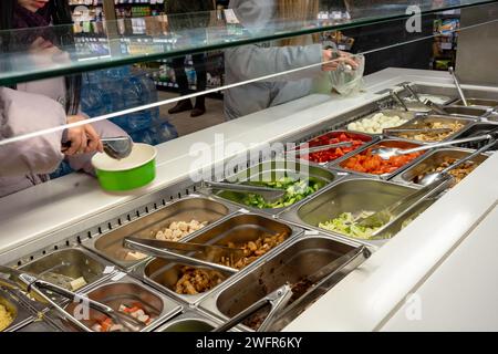 Frischer Salat Bartheke mit den Händen der Person, die Gemüse in eine Salatschüssel heben. Stockfoto