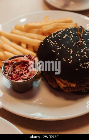 Pommes frites und ein Beef Burger mit einem schwarzen Brötchen in einem Café. Amerikanisches köstliches Mittagessen Stockfoto