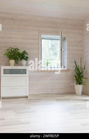 Offenes Fenster in einem Raum mit Pflanzen und einer Kommode in einem Holzhaus Stockfoto