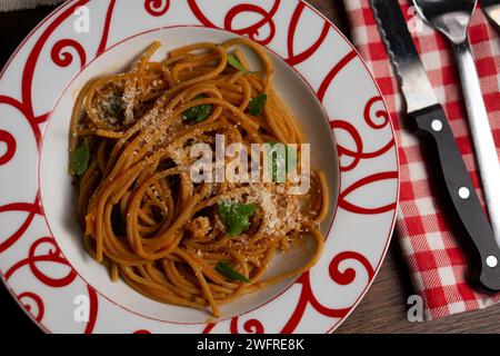 Hausgemachte Spaghetti mit Basilikum- und Tomatensauce, geriebenem Käse und strukturierten Sojabohnen. Es liegt auf einer rot-weißen Schüssel, das Besteck auf der Seite Stockfoto
