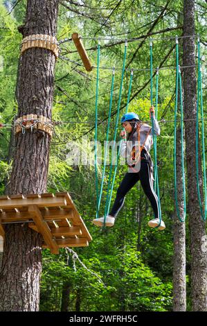 Von unten ein Teenager-Mädchen in Sportbekleidung, das auf Hängeleiter im Abenteuerbaumpark spaziert Stockfoto