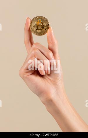 Die anonyme Frau demonstriert goldene Bitcoin vor beigefarbenem Hintergrund in hellen Studio-Kryptowährung und elektronischem Austausch und finanzprofi Stockfoto