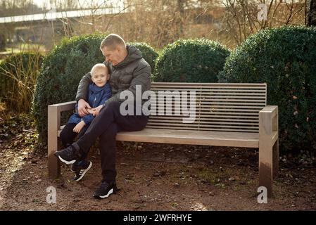 Herbstliche Familienzusammenhänge: Vater, 40 Jahre alt, und Sohn - wunderschöner 8-jähriger Junge, im Park sitzend. Stockfoto