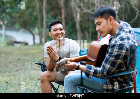 LGBTQIA Gay Paare campen zusammen im Wald für Urlaub und entspannen auf der Gitarre zusammen Stockfoto