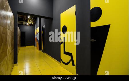 Schwarzer und gelber Flur mit Türen zu Toiletten: Weibliche, männliche und zugängliche Toilette. Gelber Fliesenboden und dunkle Holzkohlewände. Stockfoto